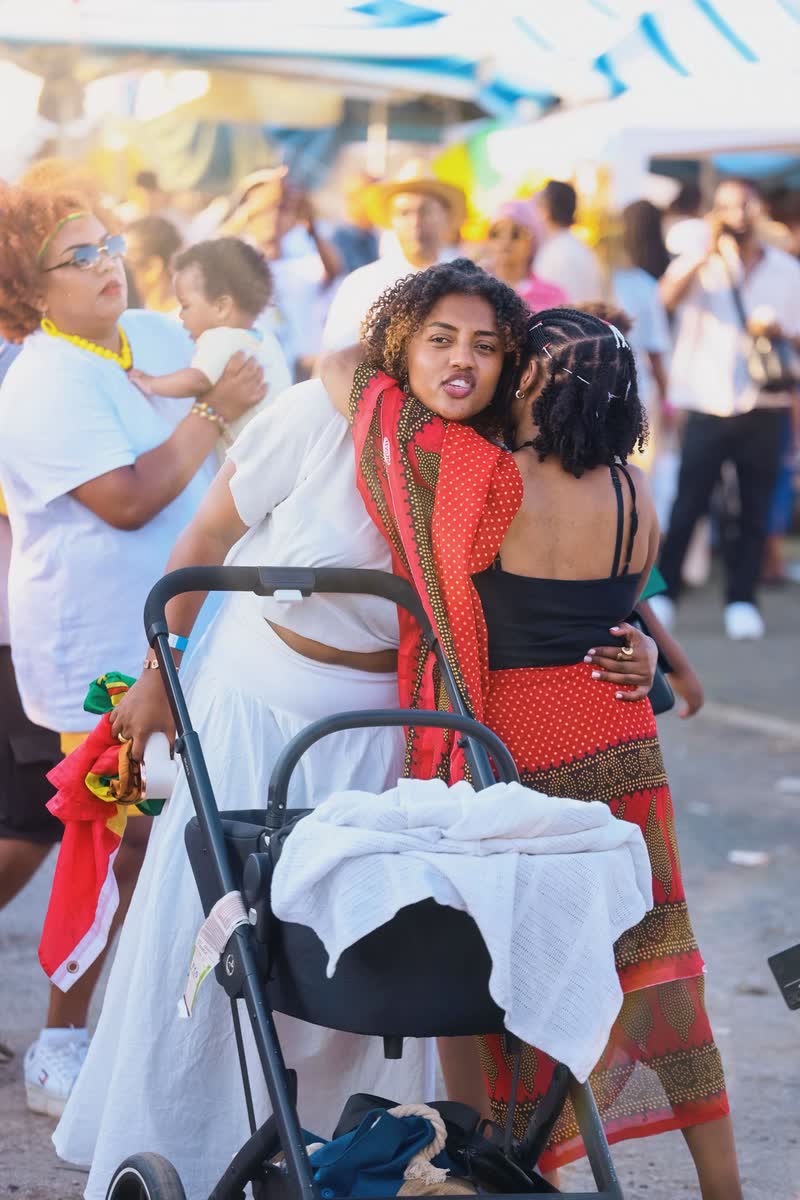Two women embracing at an ESCFE gathering, families and a pushchair nearby